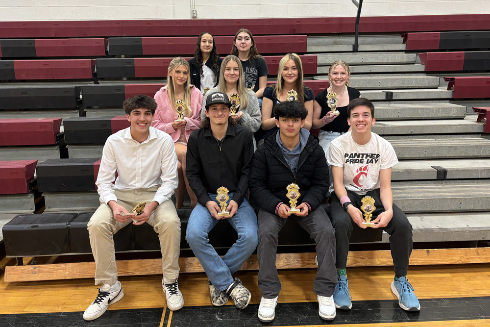 Winter sports award winners pose for photo holding trophies and sitting on bleachers