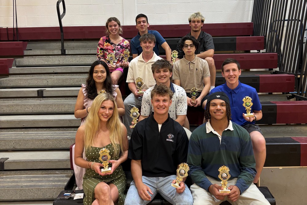 Spring sports awardees sitting on bleachers holding trophies